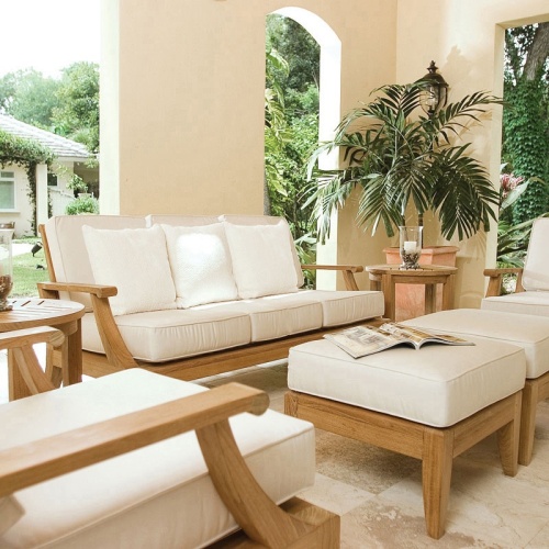 70871 Laguna 7 pc Conversation Set angled front view on outdoor patio with tray on ottoman and plant and books on side table with privacy fence and trees in background