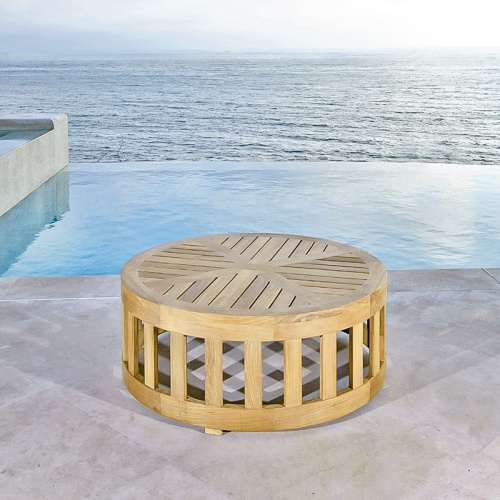 70872 Kafelonia teak 36 inch diameter round coffee table ottoman on concrete patio in front of infinity pool with ocean and sky in background