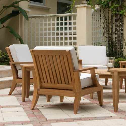 12152DP Laguna Teak Lounge Chair showing 3 chairs with 2 side tables and coffee table on paver patio with lattice fence building and trees in background