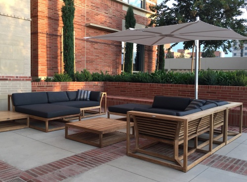 13801DP Maya Left Side Sectional Set with cushions umbrella coffee table ottoman on patio with brick planter with plants trees and brick building background