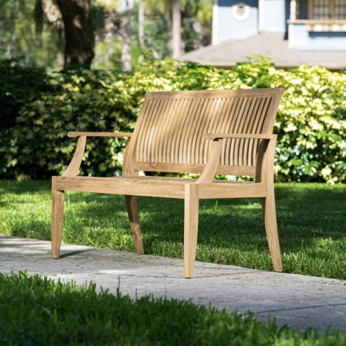 13810 Laguna 4 foot Teak Bench front angled view on concrete walkway with bushes in background