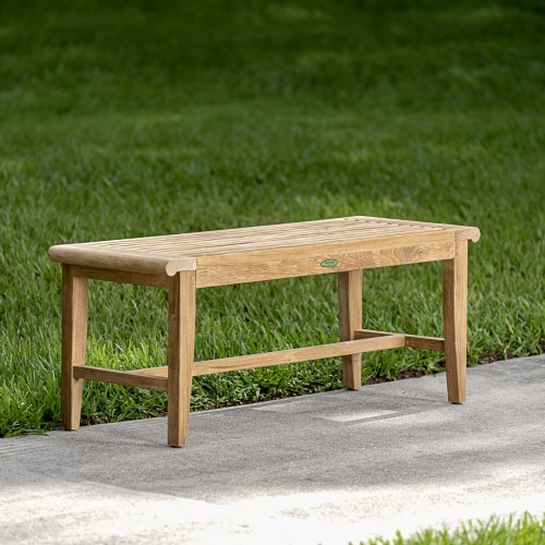 13915 Laguna 4 foot long teak Backless Bench on concrete walkway with grass and lake with fountain in background
