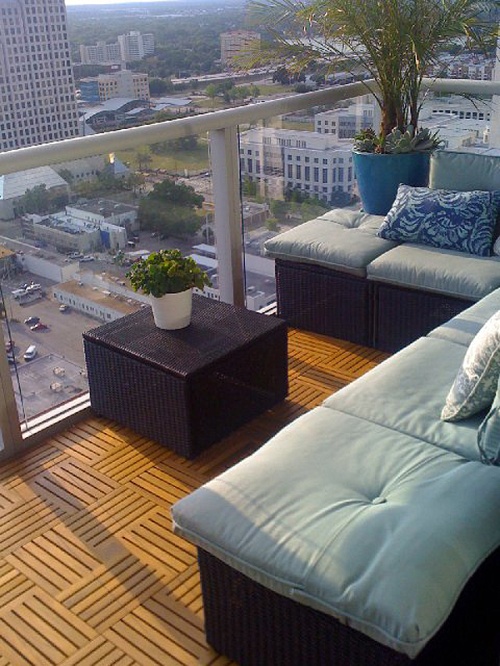 18412 parquet teak tiles assembled on a condo balcony with glass railing potted palm and flowering plant a sofa set overlooking a city view