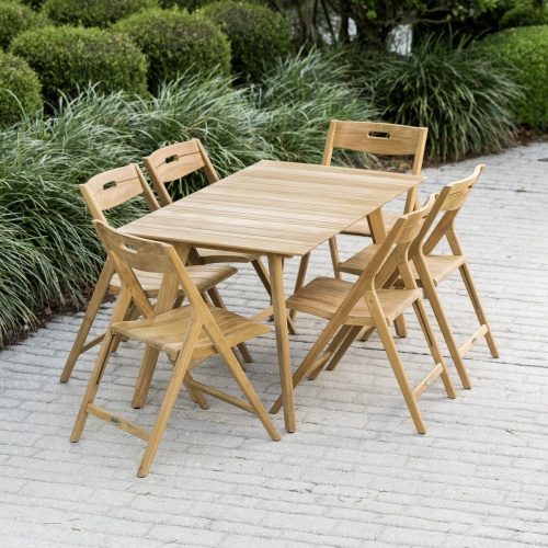 70518 Surf 7 piece teak folding Dining Set on beach with large boulders in behind dining set with ocean and blue sky background