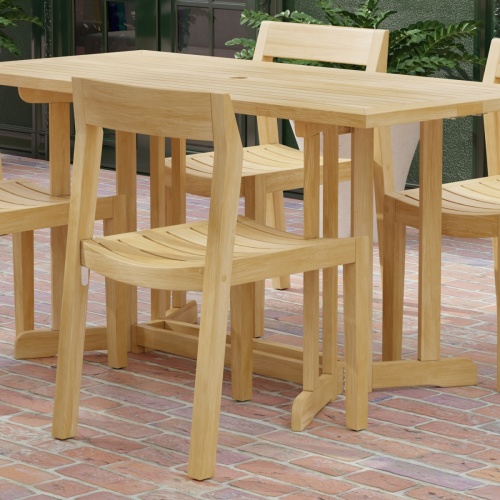 70610 Nevis Horizon Teak Wood 5 pc Dining Set showing partial angled side view on brick patio with windows and potted plants in background 