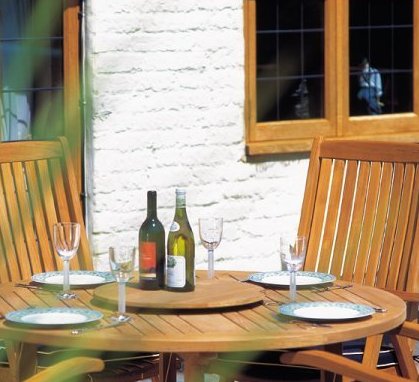 18700 teak umbrella lazy susan with two wine bottles on round table set with four plates and wine glasses with house windows and door in background