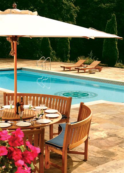 70067  Buckingham teak Curved Bench Dining Set partial view optional open market umbrella teak lazy susan two wine bottles table settings on pavers pool and landscape setting in back