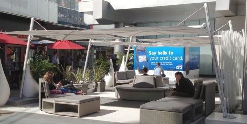SP25100SET Spectra Solo Umbrella and Paver Base on outdoor seating area of a business with people sitting walking and standing and building in background