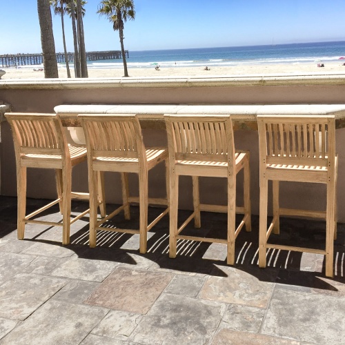 11915 laguna four teak twenty four inch height counter stool on outdoor stone patio against concrete counter looking out to the ocean with palm trees and blue sky background