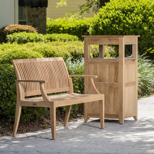 13810 Laguna 4 foot Teak Bench angled on concrete walkway with bushes in background