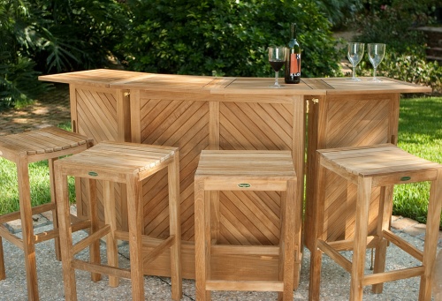 17112 Somerset teak bar and stool five piece set showing three wine glasses and wine bottle on top with stone patio a grass area paver walkway and lush tropical plants in background