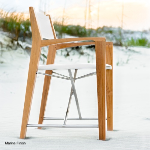 12915F Odyssey folding teak and stainless steel dining chair with Marine finish on beach with boulders and ocean and sky in background