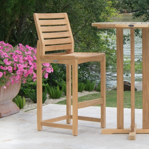 11812 Somerset Side Barstool and 30 inch Teak Bar Table on concrete patio potted flowering plant with lake and trees in background