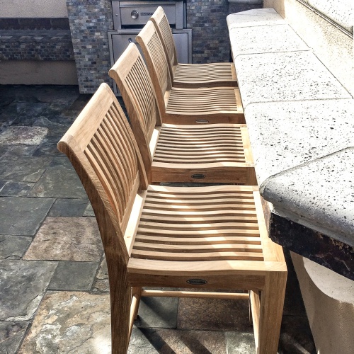 11915 laguna four teak twenty four inch height counter stool on outdoor stone patio against concrete counter side view with outdoor kitchen stone wall in background