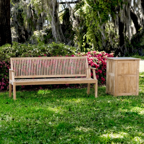 13812 Laguna 5 foot long Teak Bench beside teak Palazzo I trash receptacle on grass with flowering shrubs in background