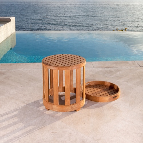 14171 Kafelonia 36 inch Teak Coffee Table Ottoman with cushion side view on stone patio with an infinity pool ocean and blue sky in background