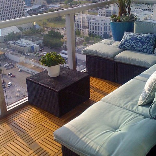 70408 Parquet 50 pack Teak 18 inch Square Deck Tiles on outdoor balcony with sectional sofa and side table with plants overlooking a city