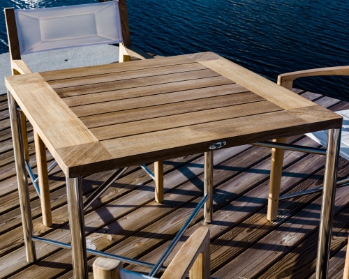 12915F Odyssey folding teak and stainless steel dining chair with Marine finish on beach with sea grass and sunset sky in background