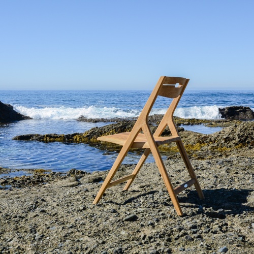 70528 Surf teak folding dining side chair left side view on beach facing ocean with blue sky in background
