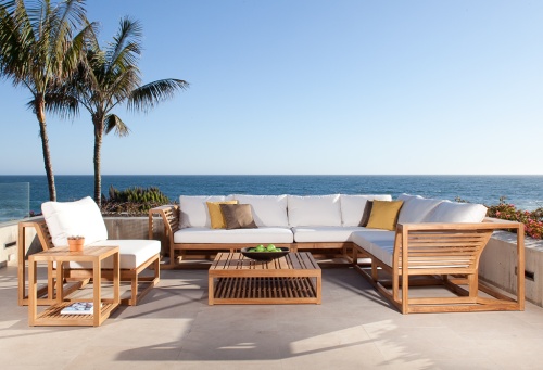 11800DP Maya teak lounge set with bowl of apples a potted plant and magazine on table shelf on concrete patio surrounded by two palm trees and plants overlooking ocean