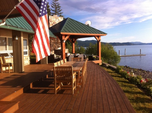 70891 Veranda grand extension table with veranda dining and side chairs on deck by lake with gazebo and US flag