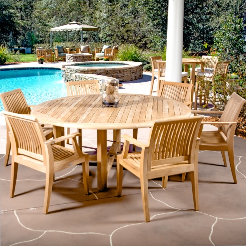 70418 Buckingham Laguna 7 piece round Dining Set in angled view with glass jar on table on stone patio with pool and hot tub and landscape plants in background