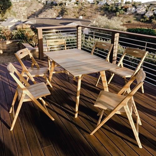 15917 Surf Teak Dining Table on wood deck in angled end view with natural vegetation in background