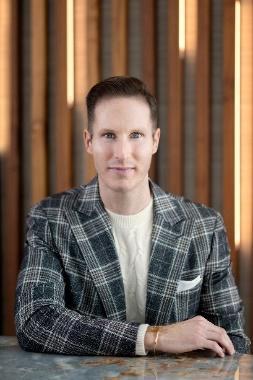 An image of Trevor Fulmer designer wearing a plaid jacket behind a desk.