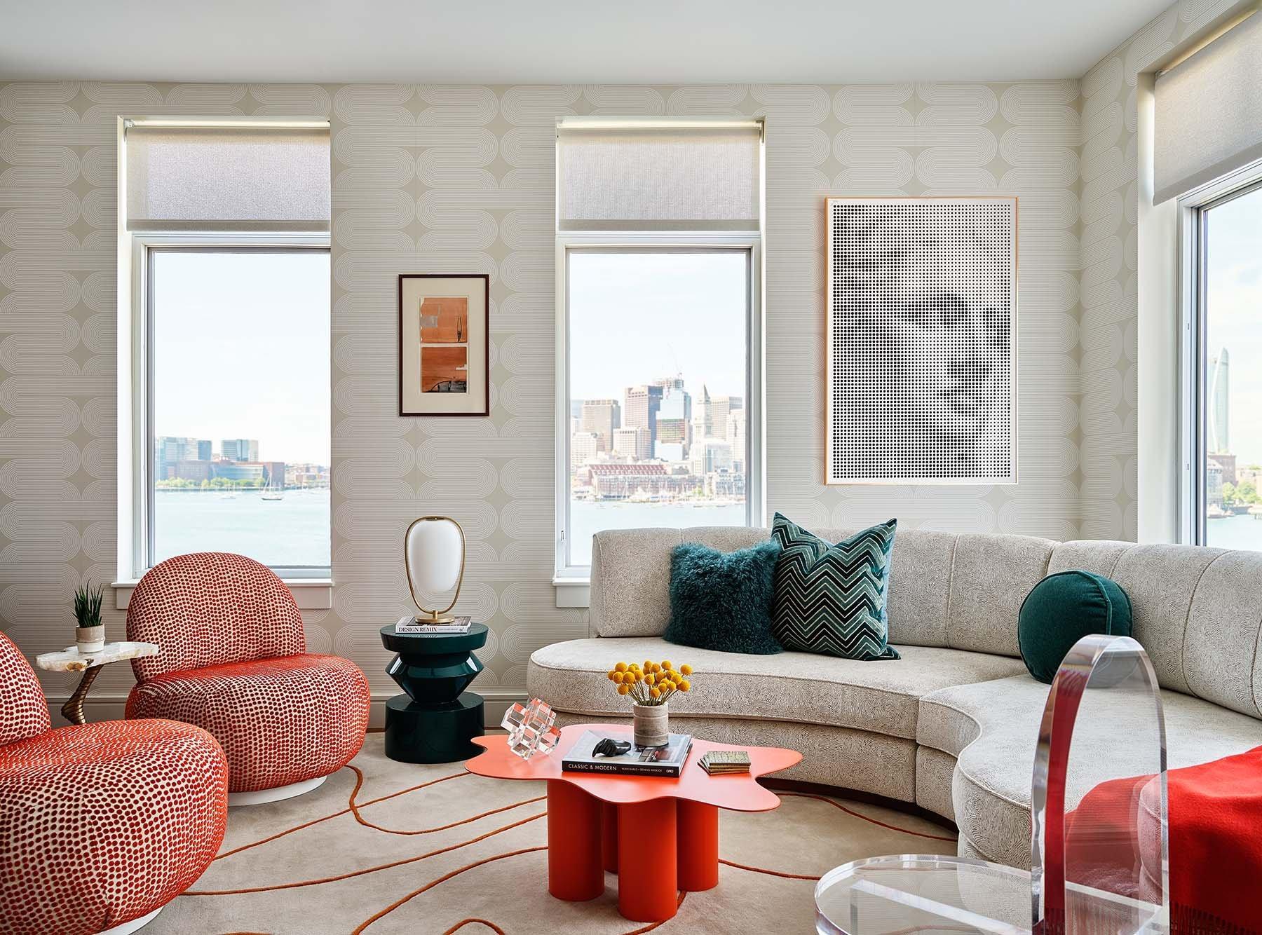 An image of Trevor Fulmer Design Vibrant Flair showing an off white semi circle sofa with green toss pillows and side table  and an orange coffee table and 2 round chairs with a city in the background.