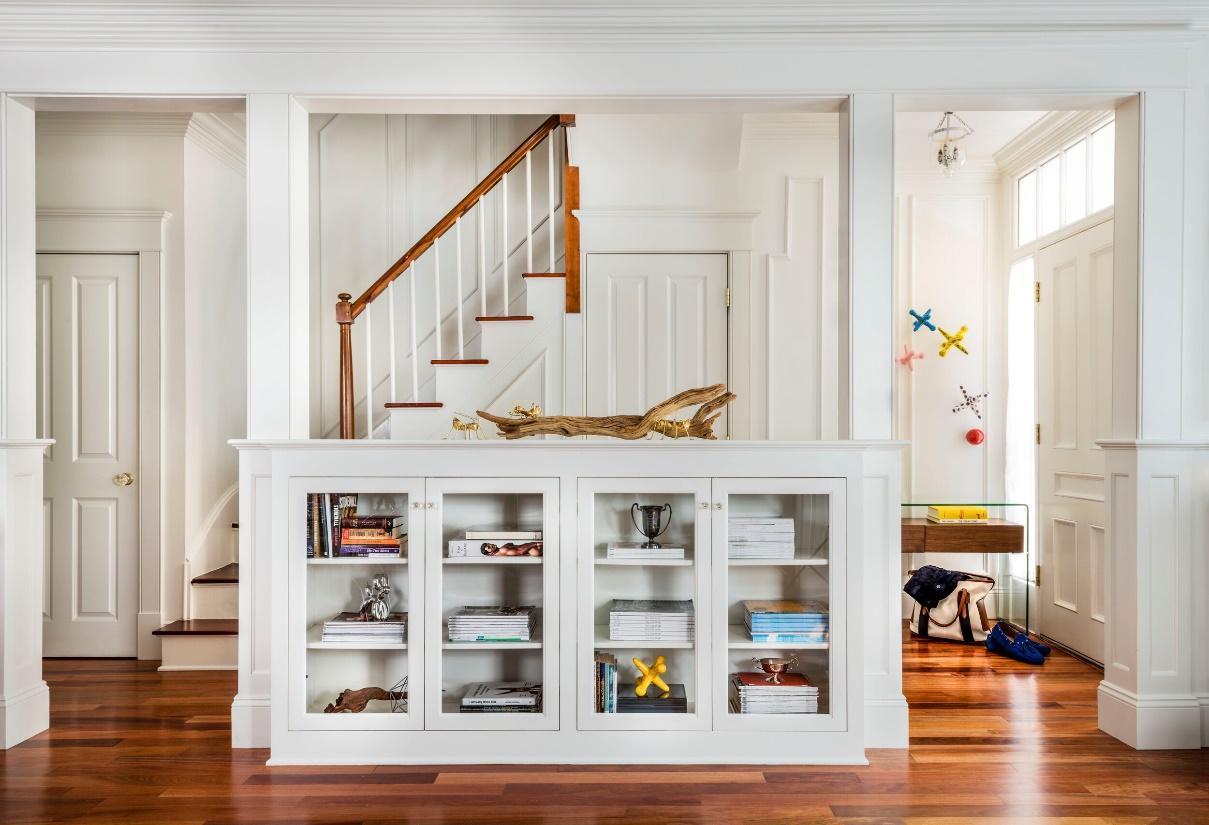 An image of an entryway and staircase leading to the upper level with a half wall with a built in bookcase.