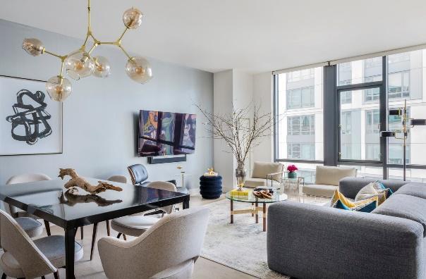 An image of a modern living room with sofa and 2 chairs and dining room set with city view in the background.