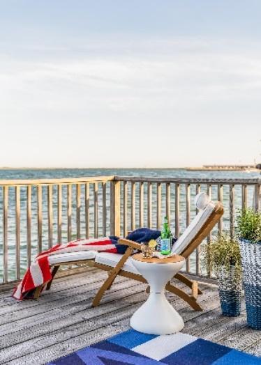 An image of Westminster Teak Barbuda Captain Steamer Lounger on an outdoor deck overlooking the ocean.
