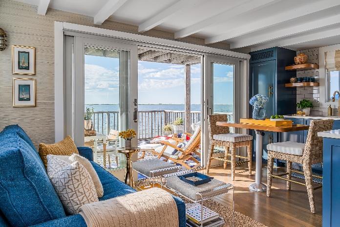 An image of the living room, dining room and kitchen of their seaside condo with French doors to the outdoor deck showing  Westminster Teak Captain Steamer and an ocean view.